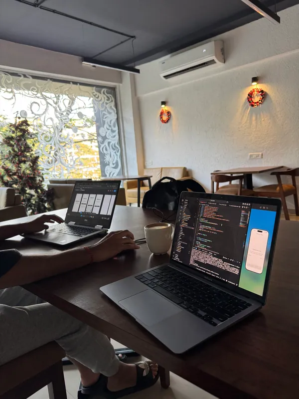 Laptops with code and a mobile app simulator at a cafe table