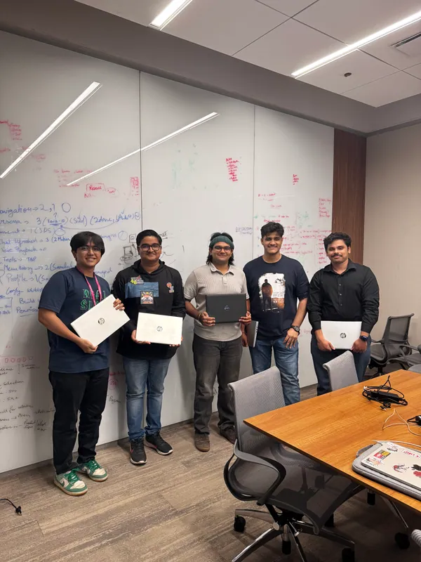 Five teammates holding laptops in front of a whiteboard